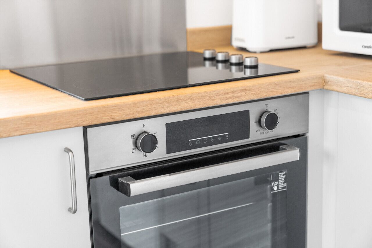 Une cuisine moderne dotée d’un four et d’une plaque de cuisson encastrés, d’appareils électroménagers en acier inoxydable et de plans de travail en bois.