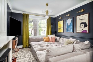 A modern living room with a sectional sofa, a flat-screen TV, and a large window with curtains.