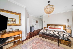 A bedroom with a wooden bed, a large mirror, a television, and a chandelier.