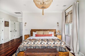 Een slaapkamer met een groot bed, een houten hoofdeinde, een kroonluchter en een raam met gordijnen.