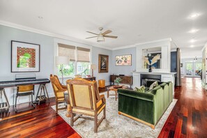 A spacious living room with hardwood flooring, a green sofa, a piano, and a fireplace.