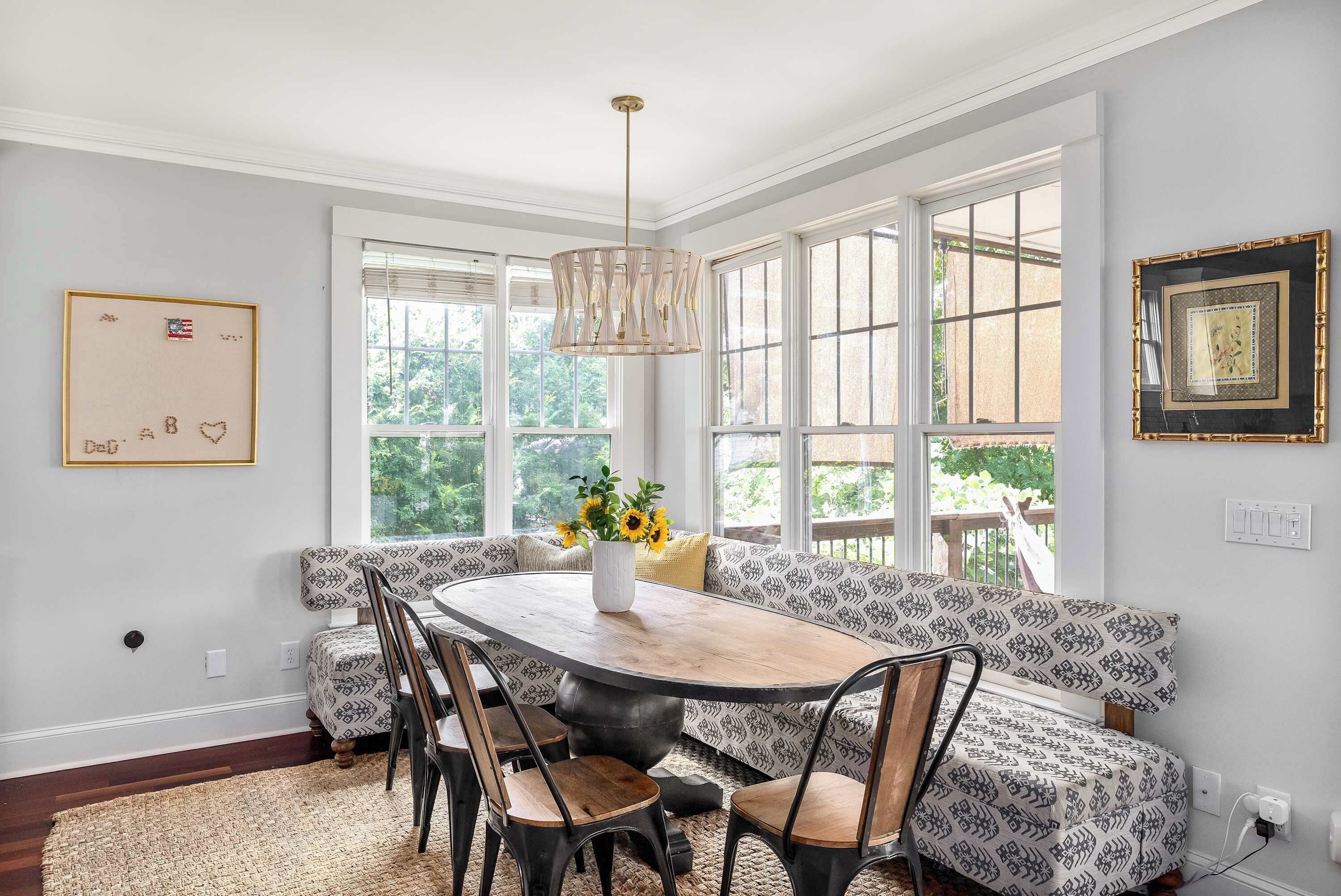 A dining area with a wooden table, patterned chairs, and a bench with a vase of sunflowers.