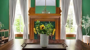 Una habitación con una mesa de madera, un jarrón blanco con flores y una chimenea con un marco de ladrillos verdes.