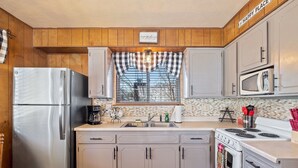 Una cocina con armarios de madera, un refrigerador de acero inoxidable, un microondas, una estufa y una ventana con cortina a cuadros.
