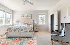 A bedroom with a bed, a chair, a nightstand, a ceiling fan, and a window. - DownWinder- Spacious 3 BR House - Walk to Beach (Kitty Hawk)
