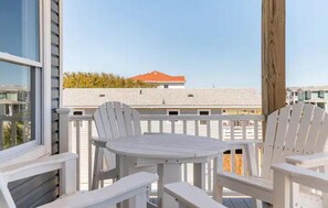 A balcony with white Adirondack chairs and a small table, overlooking a building with a red roof. - DownWinder- Spacious 3 BR House - Walk to Beach (Kitty Hawk)