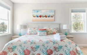 A bedroom with a bed, two bedside tables, a painting, and a window. - DownWinder- Spacious 3 BR House - Walk to Beach (Kitty Hawk)