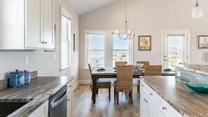 A spacious kitchen with a large island, white cabinetry, and a view of the city. - DownWinder- Spacious 3 BR House - Walk to Beach (Kitty Hawk)
