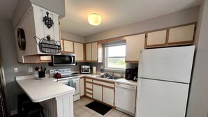 A compact kitchen with white cabinetry, a microwave, a stove, a sink, and a refrigerator. - KH Escape! Pool+Tennis+Basketball+0.8 mi to Beach! (Kitty Hawk)