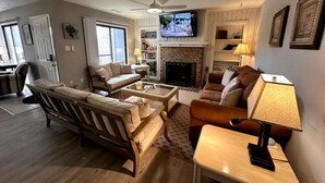 A living room with a fireplace, a television, and a ceiling fan. - KH Escape! Pool+Tennis+Basketball+0.8 mi to Beach! (Kitty Hawk)