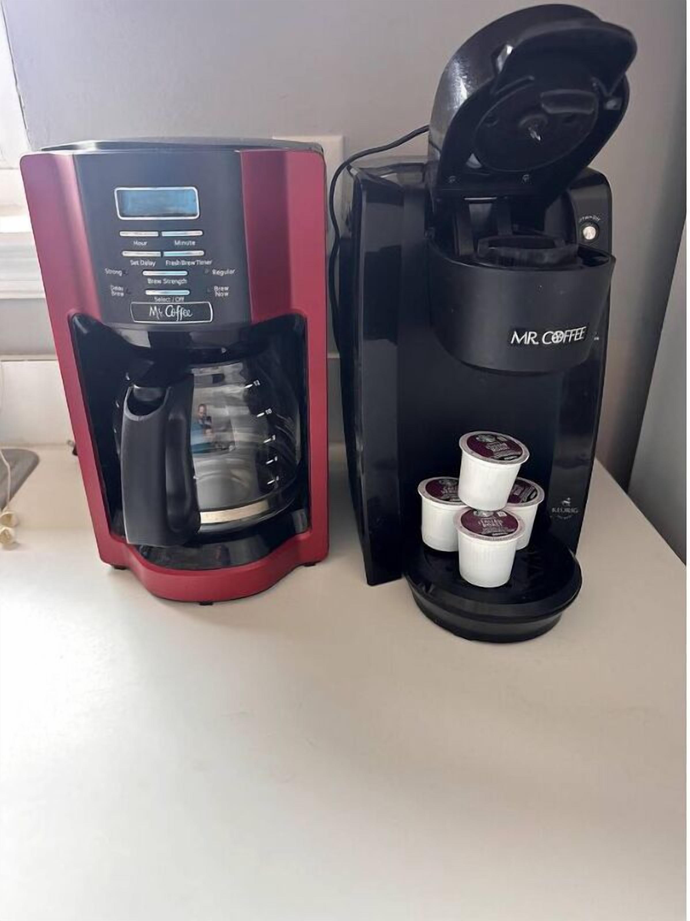 Deux machines à café, une rouge et une noire, avec plusieurs dosettes de café.