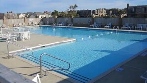 A rectangular swimming pool with a clear blue water surface, surrounded by lounge chairs and a wooden deck. - KH Escape! Pool+Tennis+Basketball+0.8 mi to Beach! (Kitty Hawk)