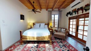 Un dormitorio con cama, ventilador de techo, ventana y alfombra estampada.