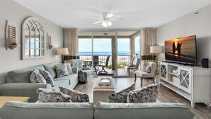 A spacious living room with a large sofa set, a television, and a view of the ocean through the glass doors. - 🌊Beach Front~Gated~ Tennis~Pools~Magnolia House #510- Gone Gulfin' (Destin)