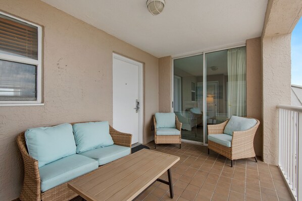 Un balcón con un sofá y dos sillones de mimbre, junto a una mesa de madera.