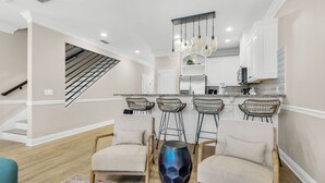 A modern kitchen with white cabinets, a central island, and a staircase leading to an upper level.