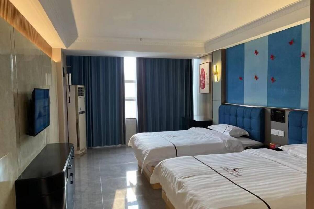 A hotel room with two beds, a flat-screen TV, a desk, and a window with curtains.