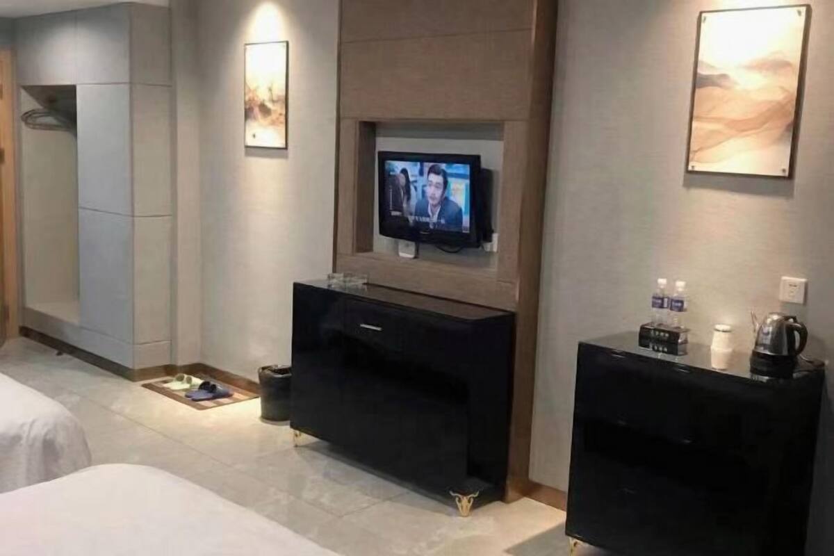 A hotel room with a television mounted on the wall, a minibar, and a coffee machine.