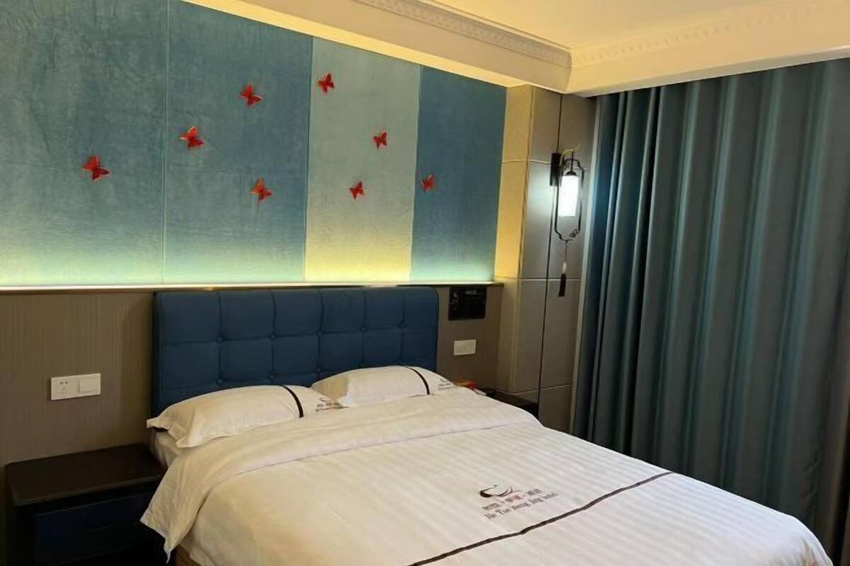 A hotel room with a large bed, a headboard, a bedside table, and a wall with a decorative panel.