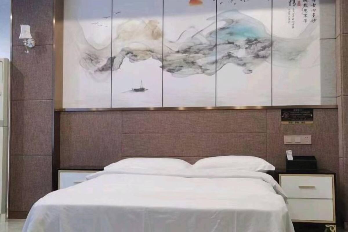 A hotel room with a bed, a nightstand, a wall-mounted artwork, and a plaque.