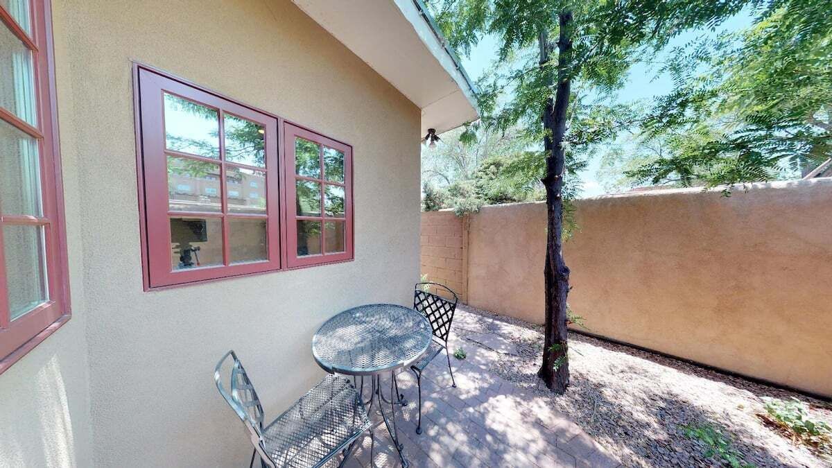 A patio with a table and chairs, a window with red trim, and a tree.