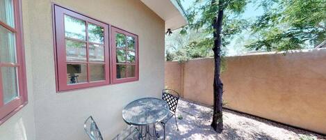 A patio with a table and chairs, a window with red trim, and a tree.