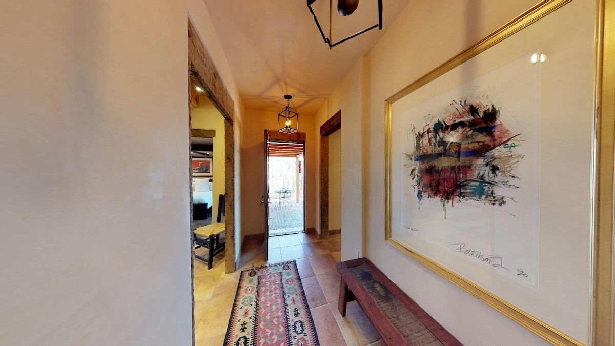 A hallway with a bench, a rug, and a framed abstract painting on the wall.