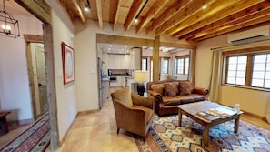A spacious living area with a high wooden ceiling, a leather sofa, a coffee table, and a patterned rug.
