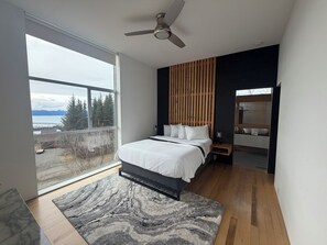Ein modernes Schlafzimmer mit Bett, Deckenventilator, großem Fenster und Blick ins Freie.