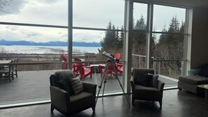 Amplia habitación con ventanas grandes, un telescopio y sillones Adirondack rojos.