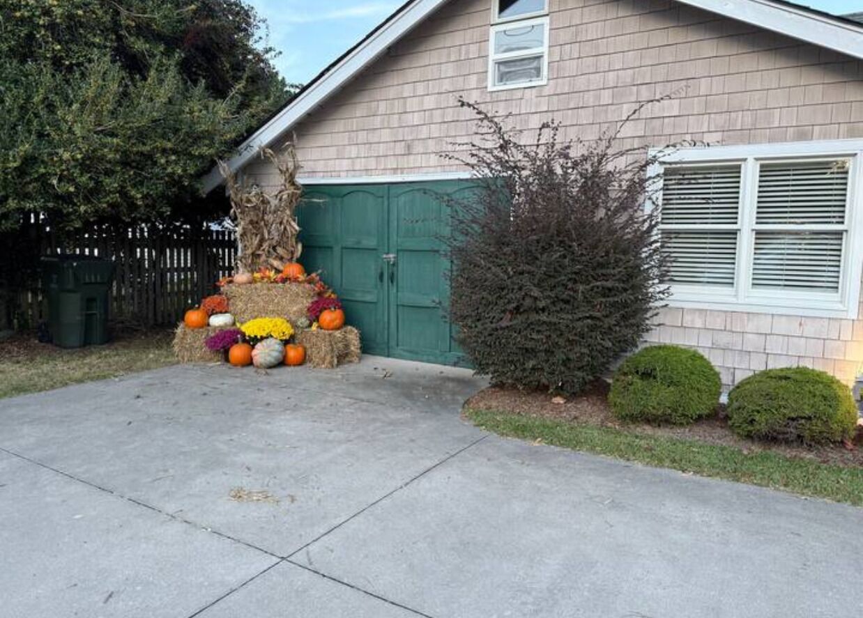 Una casa amb una porta de garatge, un arbre petit i una decoració de testos i flors al davant.