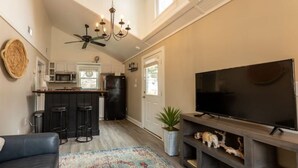 Una sala de estar moderna con sofá, mesa de centro, televisor y una cocina que incluye refrigerador, microondas y taburetes de bar.