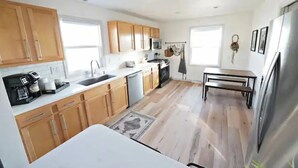 A modern kitchen with wooden cabinets, a stainless steel refrigerator, and a dining area with a table and chairs.