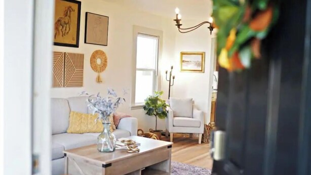 A living room with a sofa, coffee table, and armchairs. There are framed pictures on the wall and a plant on the coffee table.