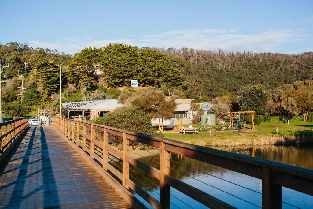 Un pont en bois enjambant une étendue d’eau calme, entouré d’une végétation luxuriante et d’un paysage vallonné.