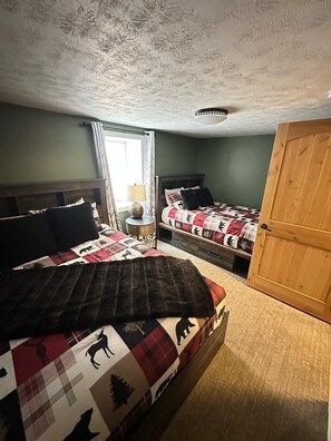 A bedroom with two beds, a wooden door, and a window with curtains. - Huge House near Pictured Rocks, Trails, Hot Tub, walking distance to Casino/Bars (Munising)