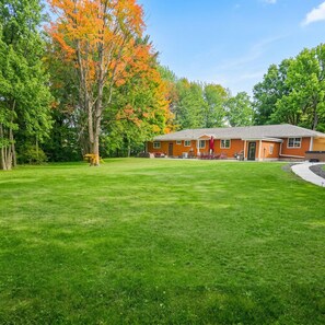 A building with a red exterior, a grassy lawn, and trees with autumn foliage. - Huge House near Pictured Rocks, Trails, Hot Tub, walking distance to Casino/Bars (Munising)