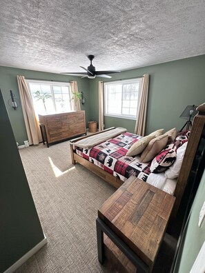 Ein Schlafzimmer mit einem Bett, einer hölzernen Bank, einem Deckenventilator und einem Fenster mit Vorhängen.