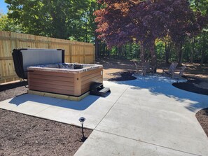 A hot tub with a wooden exterior, surrounded by a concrete patio, a wooden fence, and a tree with autumn leaves. - Huge House near Pictured Rocks, Trails, Hot Tub, walking distance to Casino/Bars (Munising)
