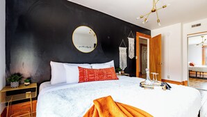 A modern bedroom with a large bed, a round mirror, a chandelier, and a black accent wall. - Jungle House Luxury Lofts – Short North High Street (Columbus)
