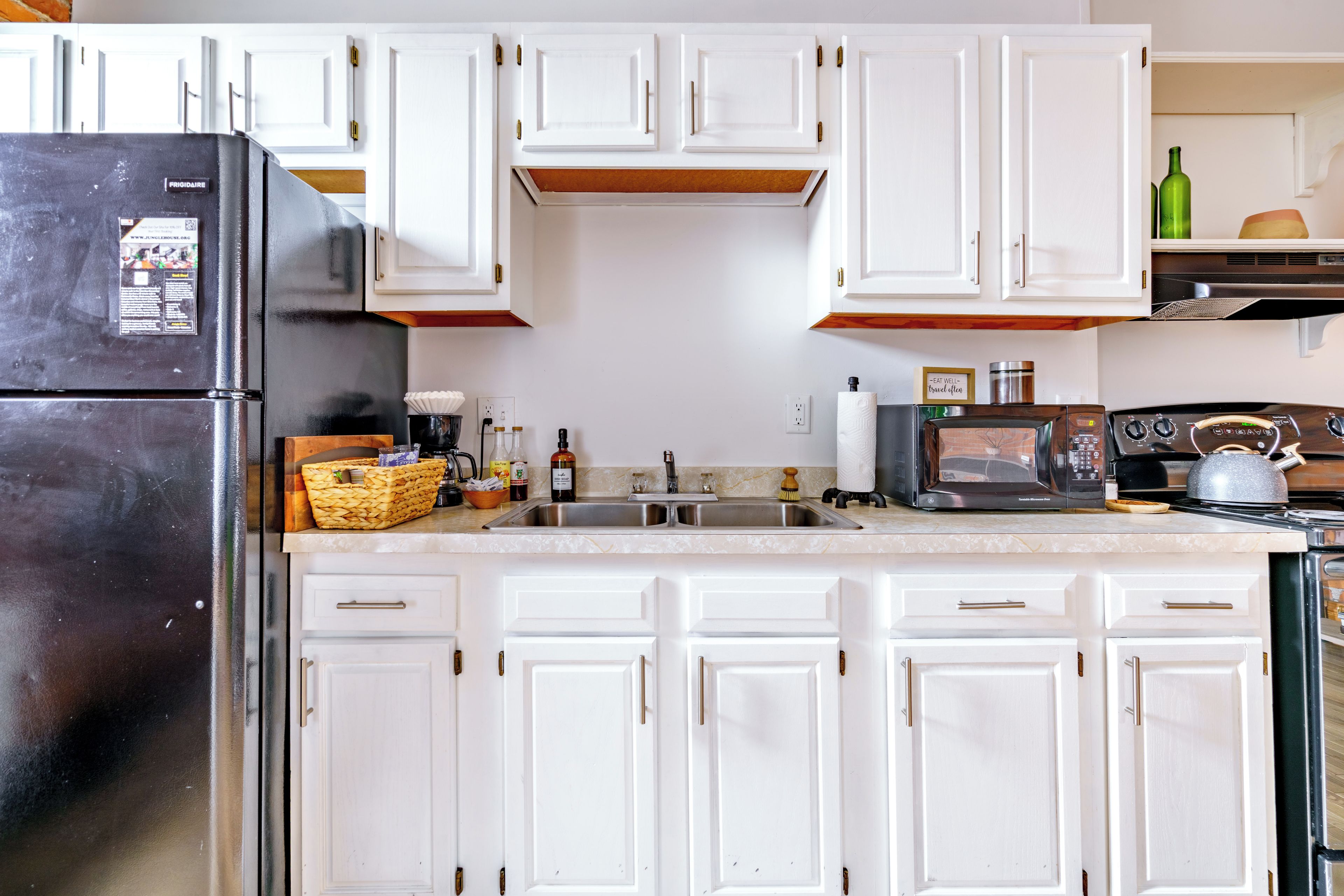 Una cocina con armarios blancos, un refrigerador negro, un microondas y una estufa.
