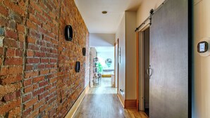 A hallway with a brick wall, wooden flooring, a door with a handle, and a thermostat on the wall. - Jungle House Luxury Lofts – Short North High Street (Columbus)