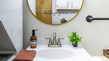 A bathroom with a white sink, a round mirror with a gold frame, a towel, a soap dispenser, and a small potted plant.