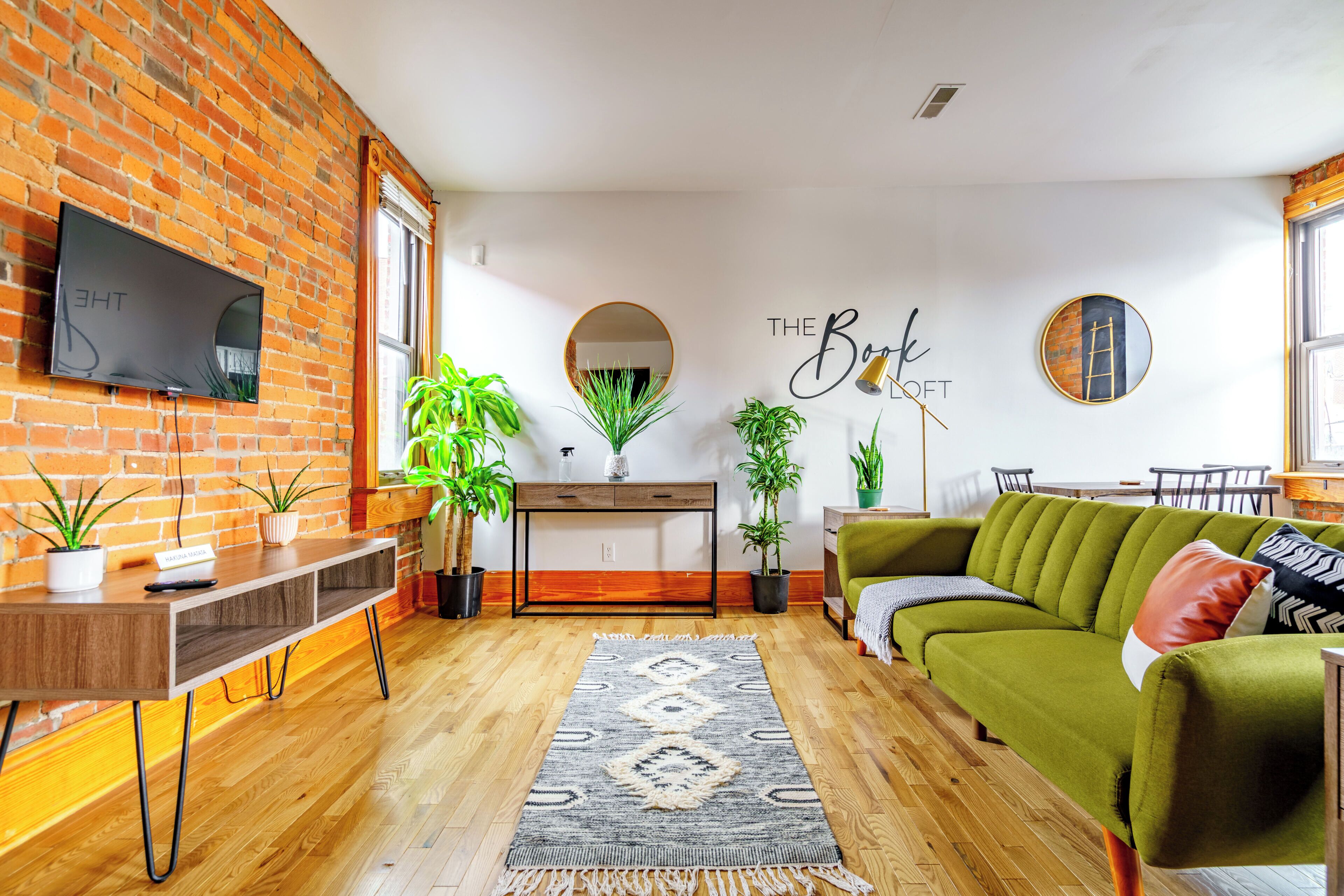 A living room with a brick wall, a flat-screen TV, a green sofa, and a wooden coffee table.