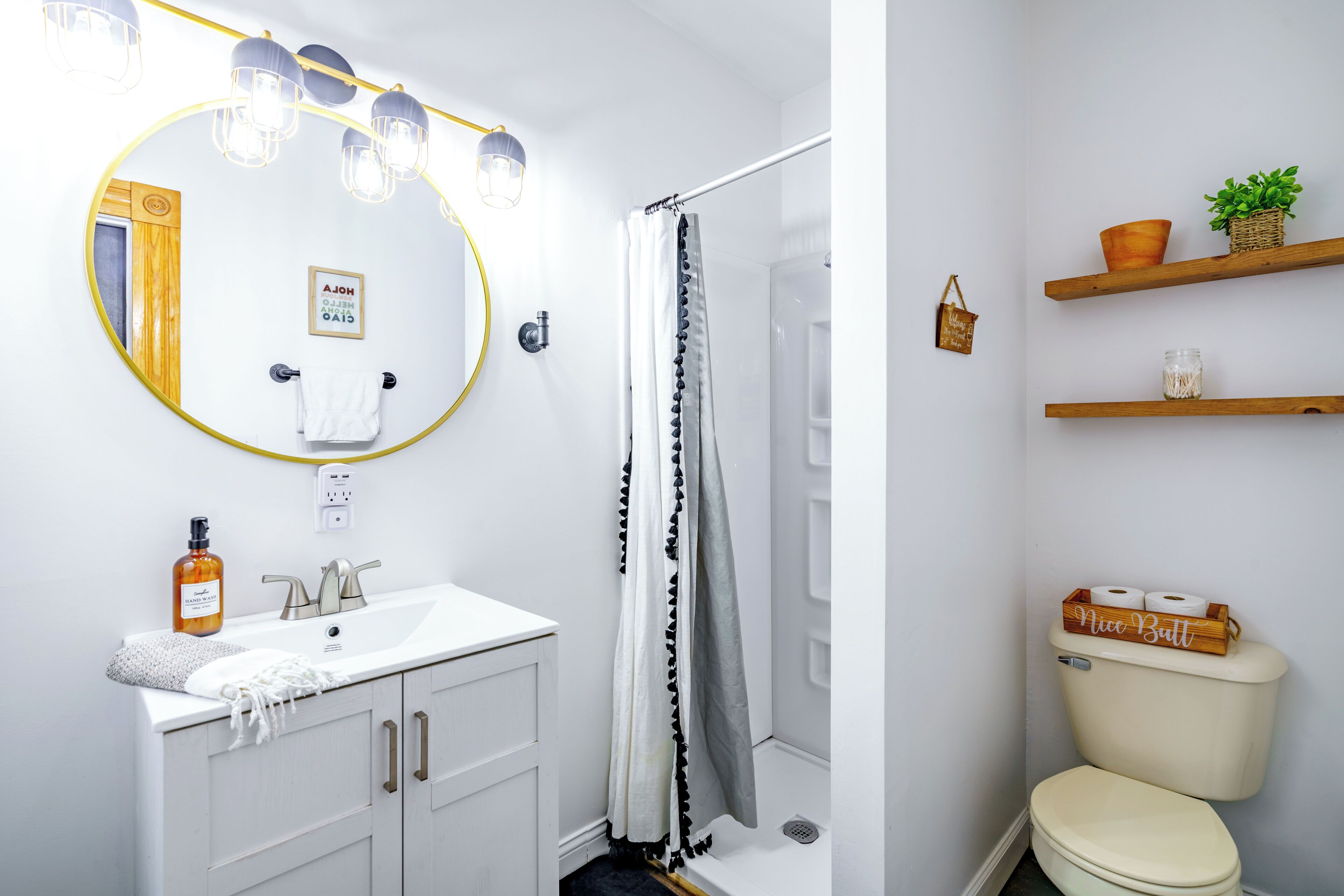 A bathroom with a white sink, mirror, and shower curtain. There are shelves with toiletries and a potted plant.