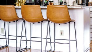 A modern kitchen with white cabinets, a central island with bar stools, and various appliances. - Jungle House Luxury Lofts – Short North High Street (Columbus)
