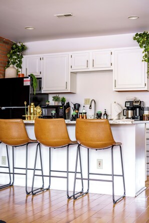 A modern kitchen with white cabinets, a central island with bar stools, and various appliances. - Jungle House Luxury Lofts – Short North High Street (Columbus)