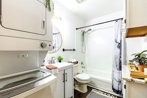 A modern bathroom with a Whirlpool washer, a toilet, a bathtub, and a shower.