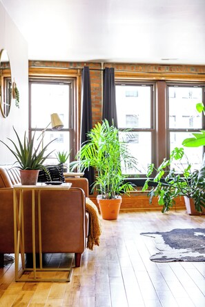 A living room with a brown sofa, a coffee table, and several potted plants. - Jungle House Luxury Lofts – Short North High Street (Columbus)