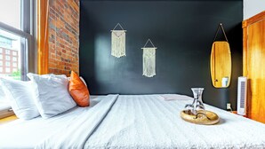 A neatly made bed with white and orange pillows, a wooden headboard, and a bedside table with a glass vase and a tray. - Jungle House Luxury Lofts – Short North High Street (Columbus)